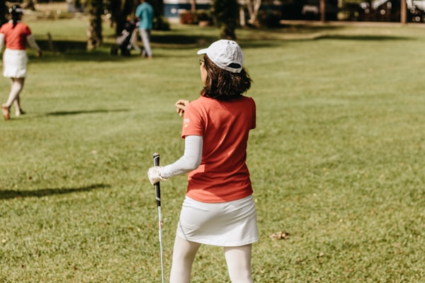 a woman in a red shirt and white skirt playing golf
